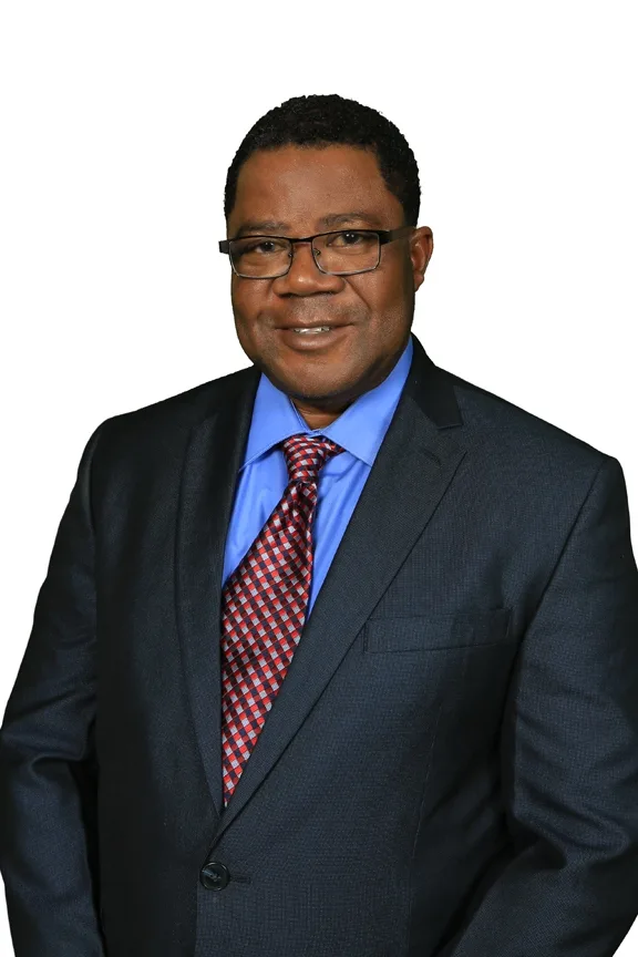 Portrait of author Shad Eddie Mongrue, smiling, in a navy suit and red patterned tie.